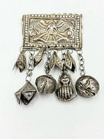 Front view of rectangular silver plaque brooch showing embossed bird motif and dangling charms