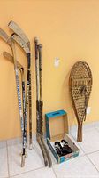 Group shot showing six hockey sticks, pair snowshoes, box with skates