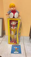 Group shot showing boxed Ronald McDonald doll, Dennis the Menace doll, Rupert cloth book