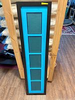 Front view showing black frame and teal mat with five openings