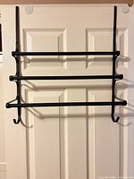 Front view of black metal over-door towel rack mounted on a door