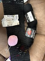 Lot overview with two black skeins, pink yarn ball, crochet strip, and pattern leaflet
