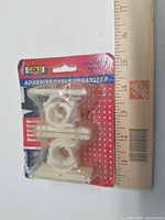 Front view of sealed package showing five off-white adhesive cable organizer clips and ruler for scale