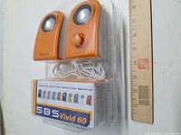 Front view of sealed package showing both orange Creative SBS Vivid 60 speakers, attached cables and volume control