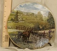 Front view of decorative plate with pastoral scene and ruler for scale