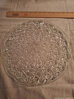 Top view of round pressed-glass platter beside ruler showing 12 in size