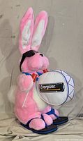 Full side view of pink Energizer Bunny plush with drum, sunglasses, flip-flops and drum sticks