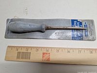 Awl on card backing with ruler for scale