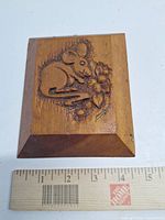 Front view of carved wooden plaque with mouse design beside ruler for scale