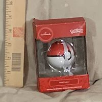 Front of boxed Pokémon Poké Ball ornament beside ruler