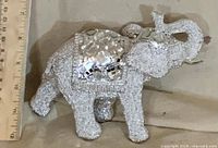Right side view of silver beaded elephant figurine next to ruler for scale