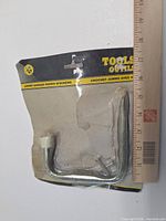Front of sealed package showing two metal hooks and screws with ruler for scale