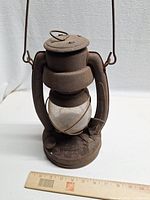 Front view of rusty metal kerosene lantern with glass globe and ruler showing height