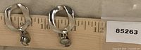 Front view of both silver-tone wavy clip-on earrings on ruler showing 1 inch height
