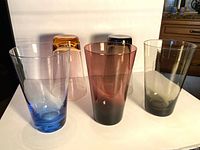 Front view of five tall coloured glass tumblers including blue, purple, two grey, amber plus inverted amber and grey tumblers
