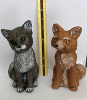 Concrete cat and fox statues beside ruler showing 9 in. height