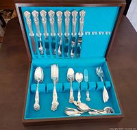 Magnolia pattern flatware arranged in wooden chest