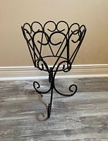 Full view of wrought iron plant stand on floor showing scrollwork basket and tripod legs