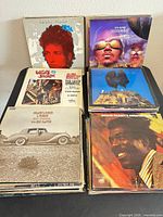 Stacks of vinyl records showing Bob Dylan Biograph box, P.M. Dawn Jesus Wept, Lovin’ Spoonful Greatest Hits, Wilson Pickett’s Greatest Hits, vintage car cover album
