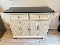 Front view of white kitchen cart showing black top, drawers, doors