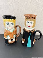 Front view of both figural mugs showing designs and faces