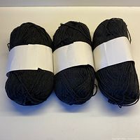 three black cotton yarn balls with paper sleeves