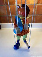 Full view of pig marionette hanging showing clothing, shoe and peg leg