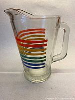 Full view of clear glass pitcher with rainbow stripes, handle and spout visible