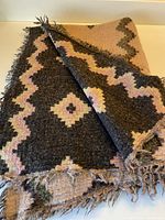 Full view of scarf showing black side with cream and rose geometric, fringed ends visible