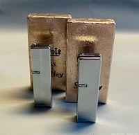Two chrome lighters standing beside gold boxes