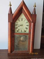 Front view showing mahogany steeple case, dial, lower glass door, brass finials