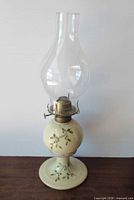 Front view of complete ceramic oil lamp showing floral design, brass burner, and glass chimney