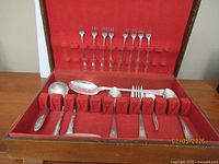 Open flatware box with forks in lid and various serving pieces in tray