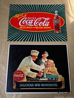 Front view of both Coca-Cola tin signs showing graphics