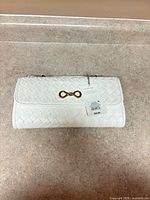 Front view of white woven faux leather clutch with gold infinity clasp and attached retail tag