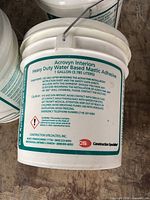 Front view of sealed 1-gallon Acrovyn Interiors water-based mastic adhesive pail showing label and capacity