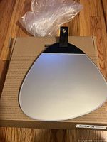 Front view of stone-shaped mirror resting on original cardboard box with plastic wrap