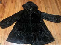 Full view of black hooded faux fur coat laid flat