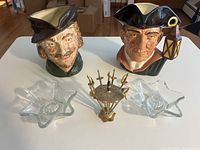 Front view of two character jugs, star glass candle holders, brass cocktail pick set