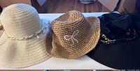 Wide shot of all three hats: cream woven wide brim, tan woven fedora, black fabric sun hat