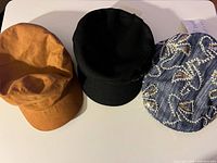 Three hats laid out: brown faux-suede, black cadet, denim embroidered