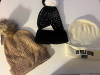 Overview of three knit beanies: tan with pom, black with rhinestones and pom, off-white with embroidery