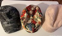 Three hats displayed: camo cadet, floral newsboy, beige sherpa newsboy