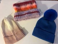 All three hats laid out: blue pom beanie, ombré ribbed beanie, fuzzy striped beanie