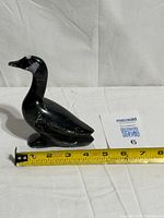 Front-side view of black stone bird with tape measure indicating length