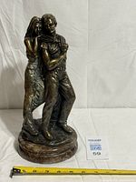 Full view of bronze lovers statue on round marble base with tape measure showing height