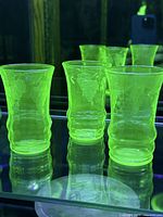 Three tumblers glowing bright green under UV light