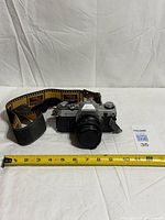 Front view of Canon AE-1 camera with lens, cap and strap next to measuring tape