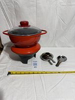 Full fondue set showing pot on base, stand, burner and snuffer with measuring tape for scale