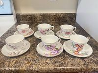 Six teacup and saucer sets displayed upright on countertop